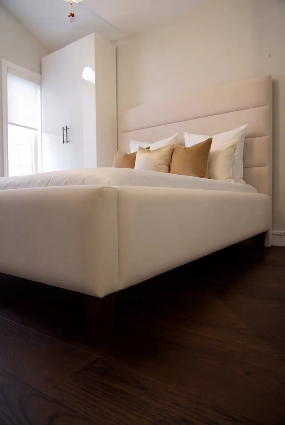 Low angled view of a sand-coloured upholstered bed with broad horizontal headboard panels.