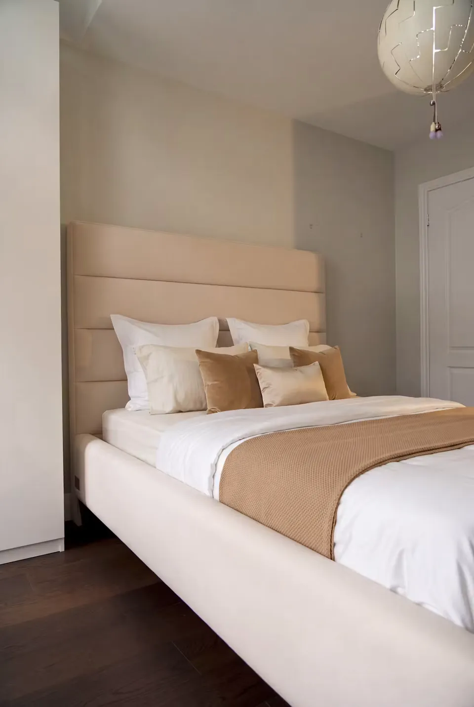 Side view of a pale upholstered bed with white bedding and ochre cushions.