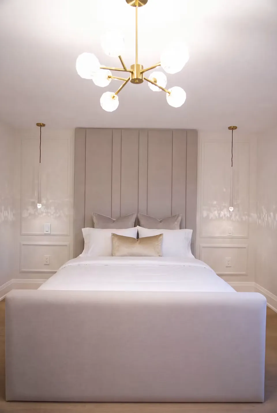 Front view of a taupe upholstered bed and tall channel headboard below a branching light