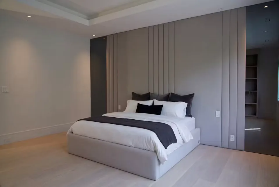 Pale upholstered bed centred on a taupe wall with narrow vertical channels