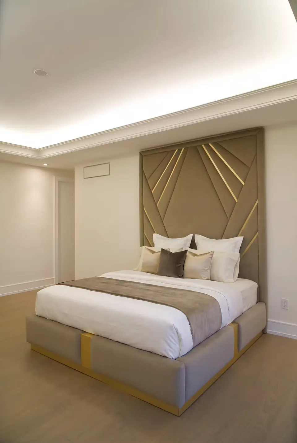 Full view of a taupe upholstered bed with a gold-edged geometric fan headboard.