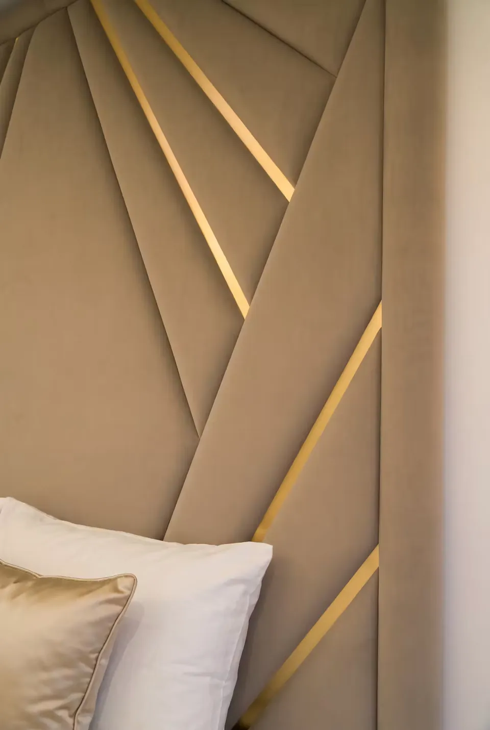 Detail of a taupe diagonal headboard panel crossed by a slender gold strip.