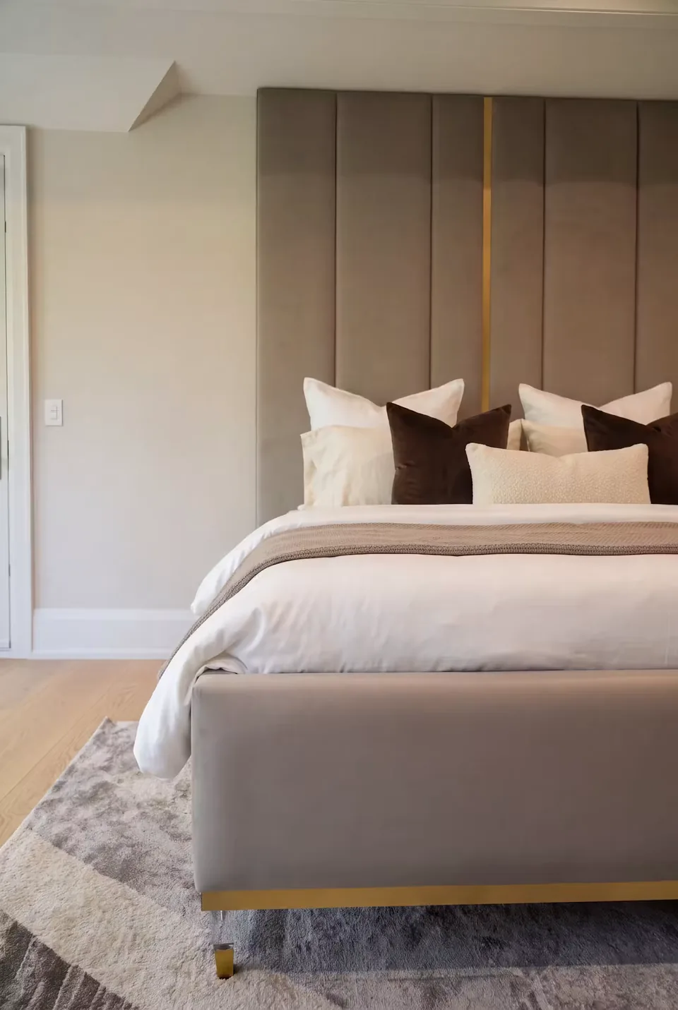 Close view of the taupe upholstered footboard and metallic trim below tall panels