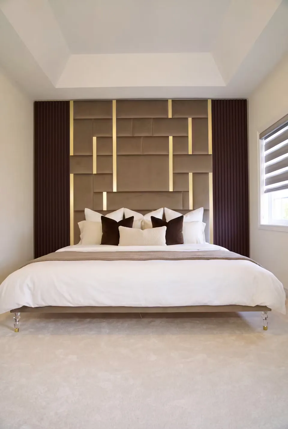 Full front view of an ivory upholstered bed beneath taupe geometric panels and gold divisions.