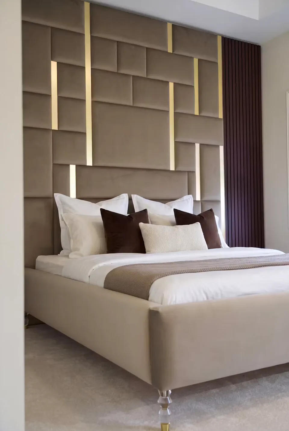 Angled view of the ivory bed frame, clear feet and tall taupe padded wall.