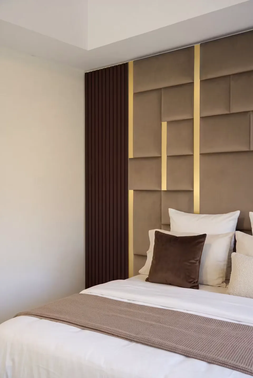 White and brown pillows against taupe wall panels bordered by dark vertical slats.