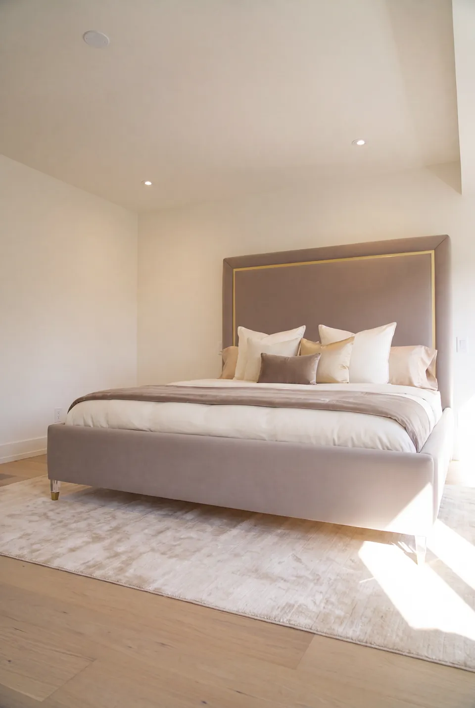 Full angled view of a taupe upholstered bed with a thin gold headboard border and metallic feet.