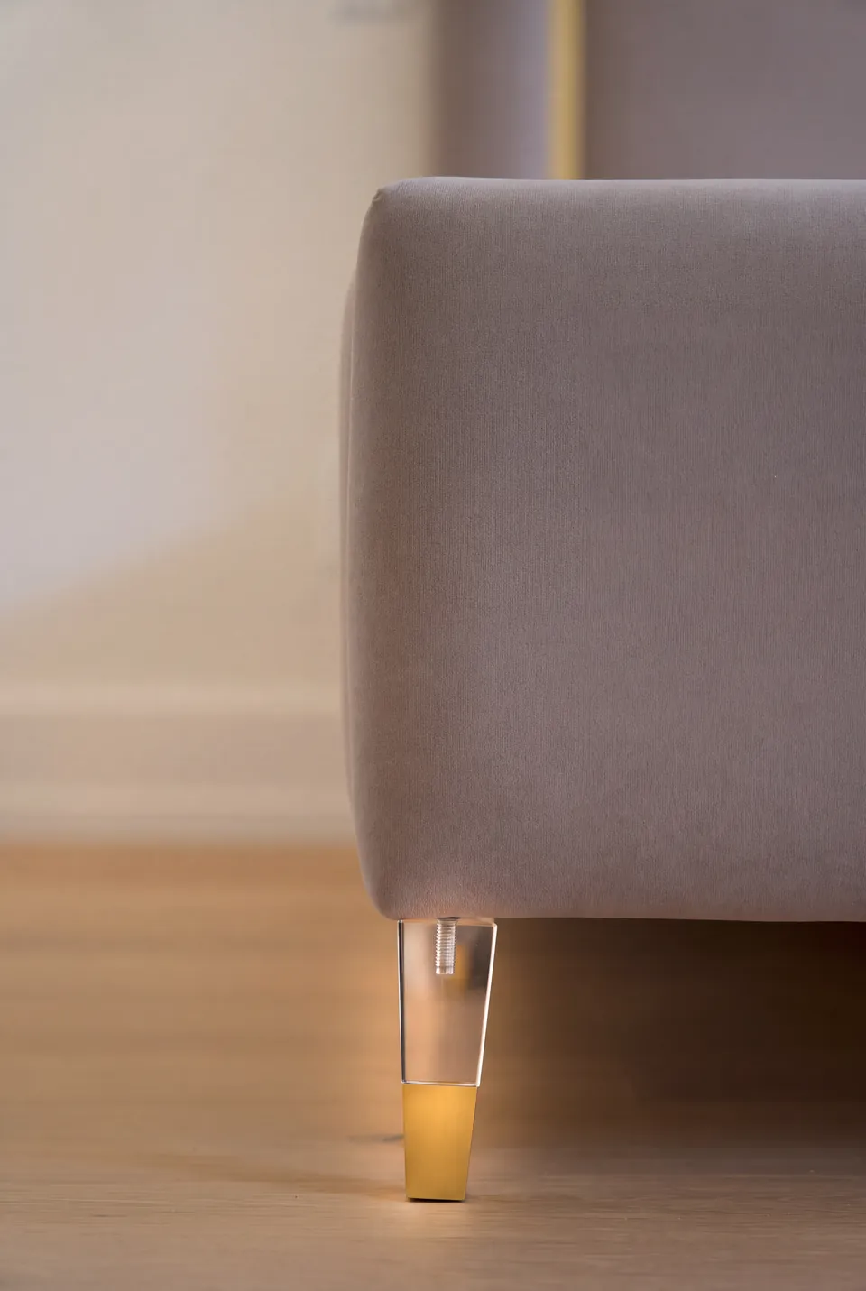 Close view of a metallic bed leg beneath the taupe upholstered frame.