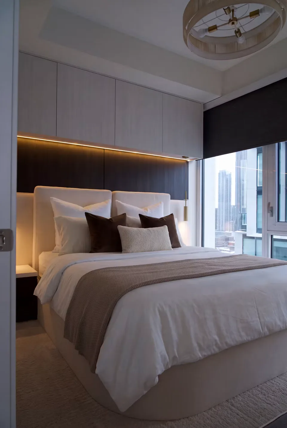 Wider view of the taupe upholstered bed beside a window under tall padded wall panels.
