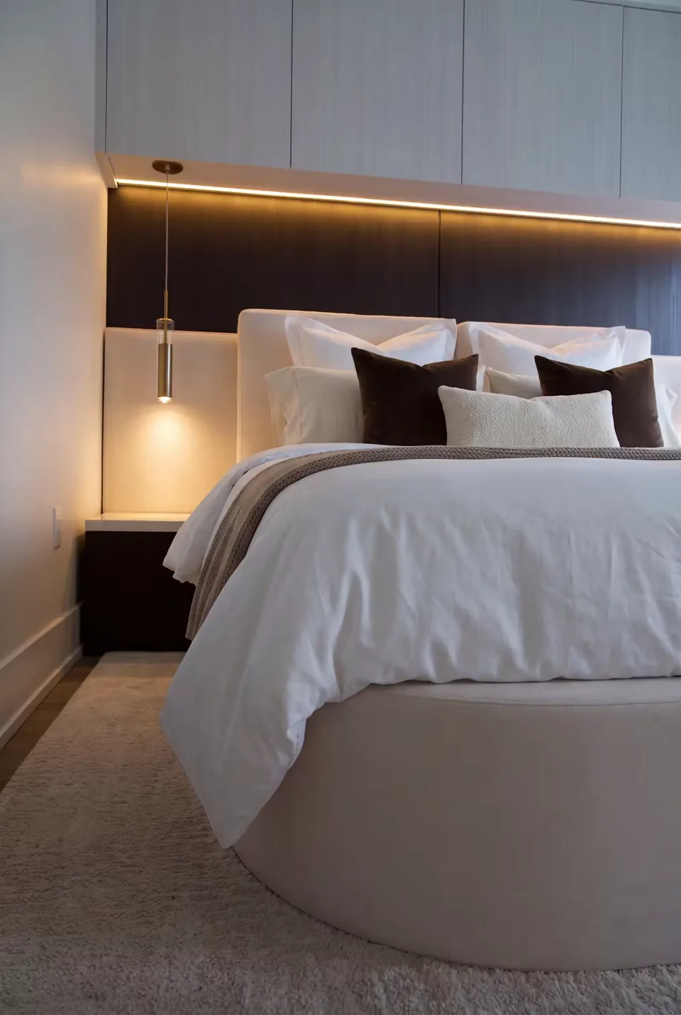 Close view of white and brown pillows against the dark horizontal headboard and amber light band.