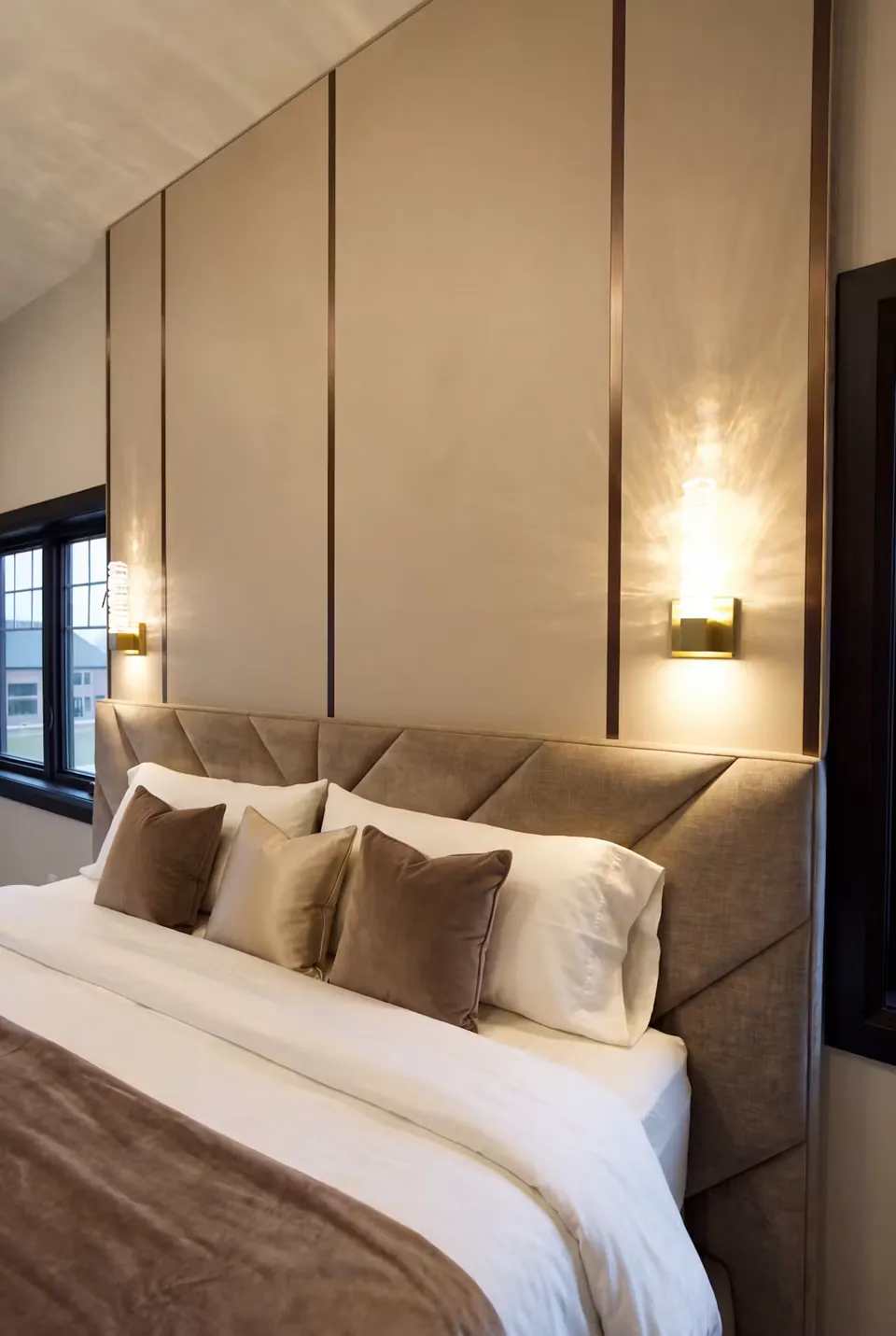 Close view of taupe upholstery, layered neutral pillows and a vertical wall light.