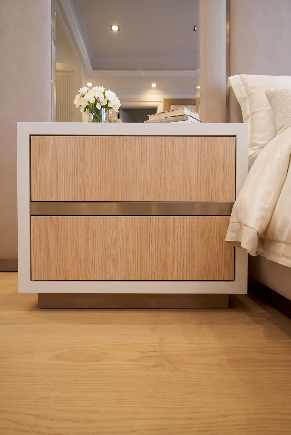 Detail of a wood-toned bedside drawer within a pale surround beside the upholstered bed.