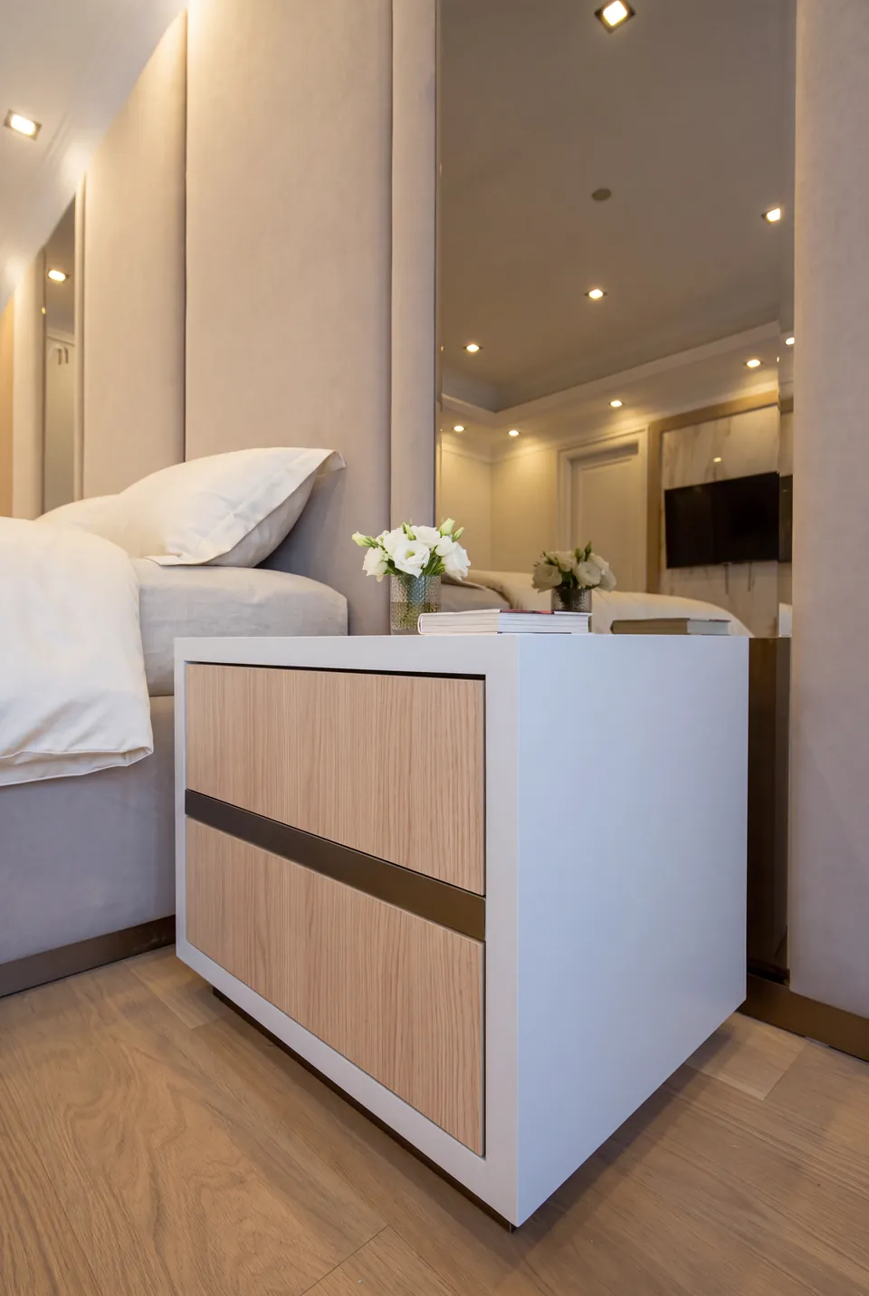 Side view of the bedside drawers, mirror and taupe upholstered wall.