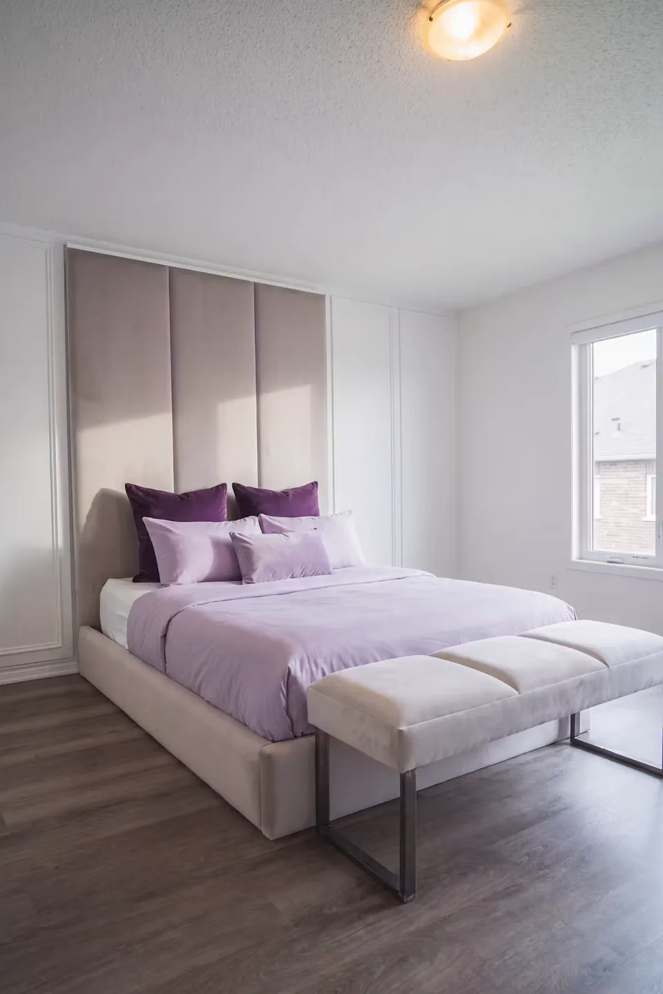 Full angled view of the taupe panel headboard, pale bed and small bench