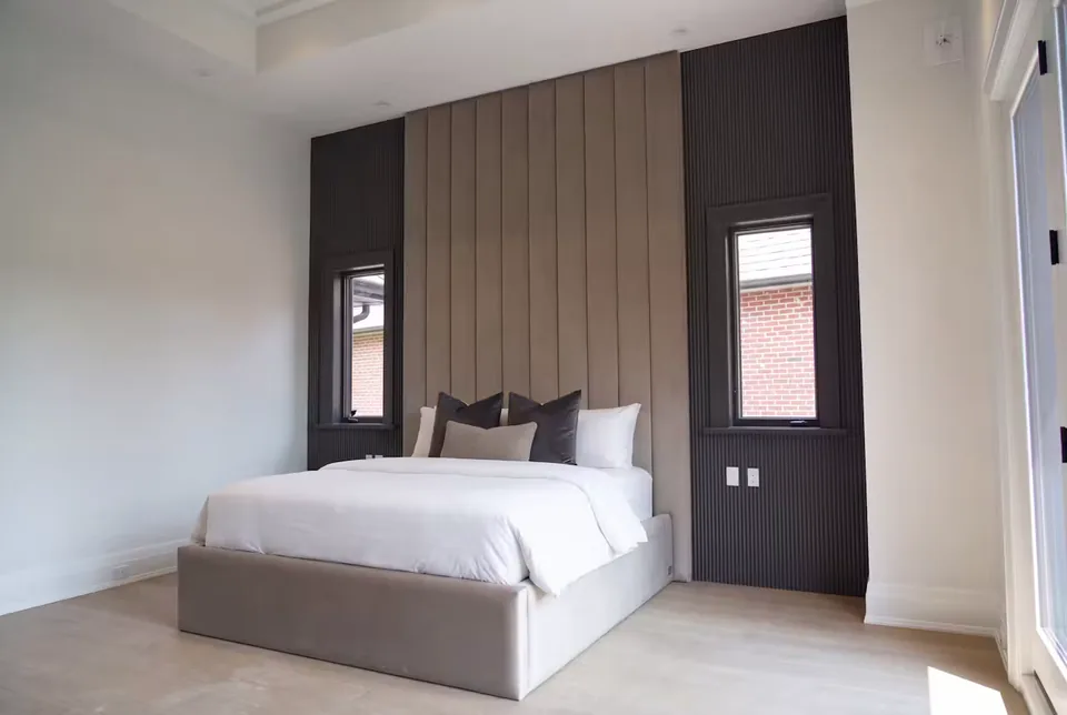 Full taupe bed beneath tall channels between two windows