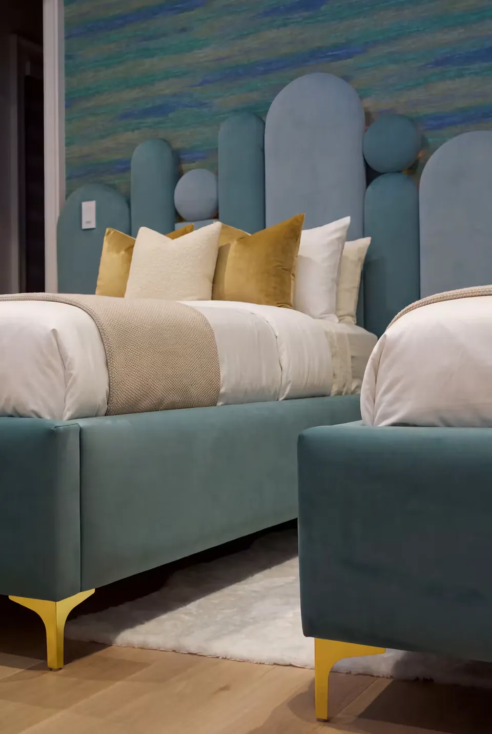 Side view of teal upholstered frames with gold-toned feet and pale bedding.
