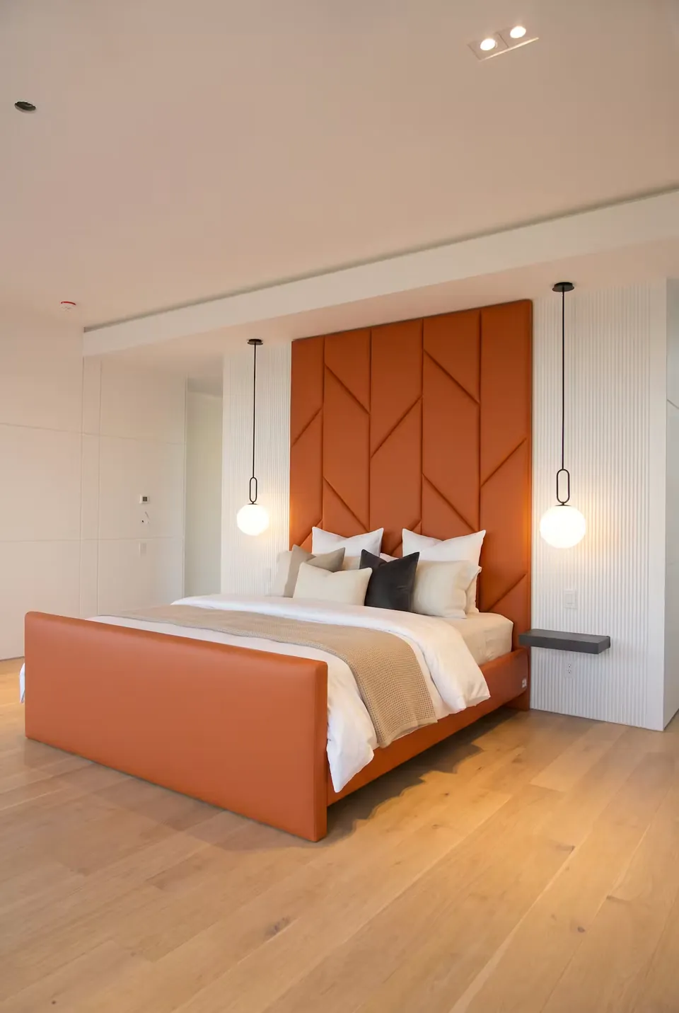 Full angled view of a terracotta upholstered bed with geometric wall panels and globe pendants.