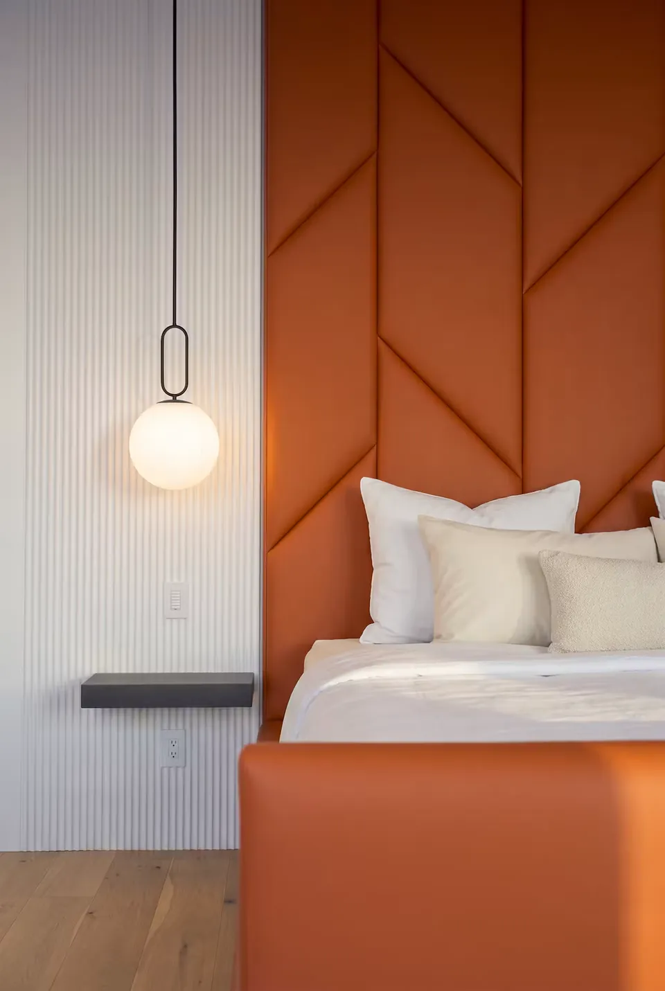 Side view of the terracotta footboard and angular headboard beside a globe pendant.