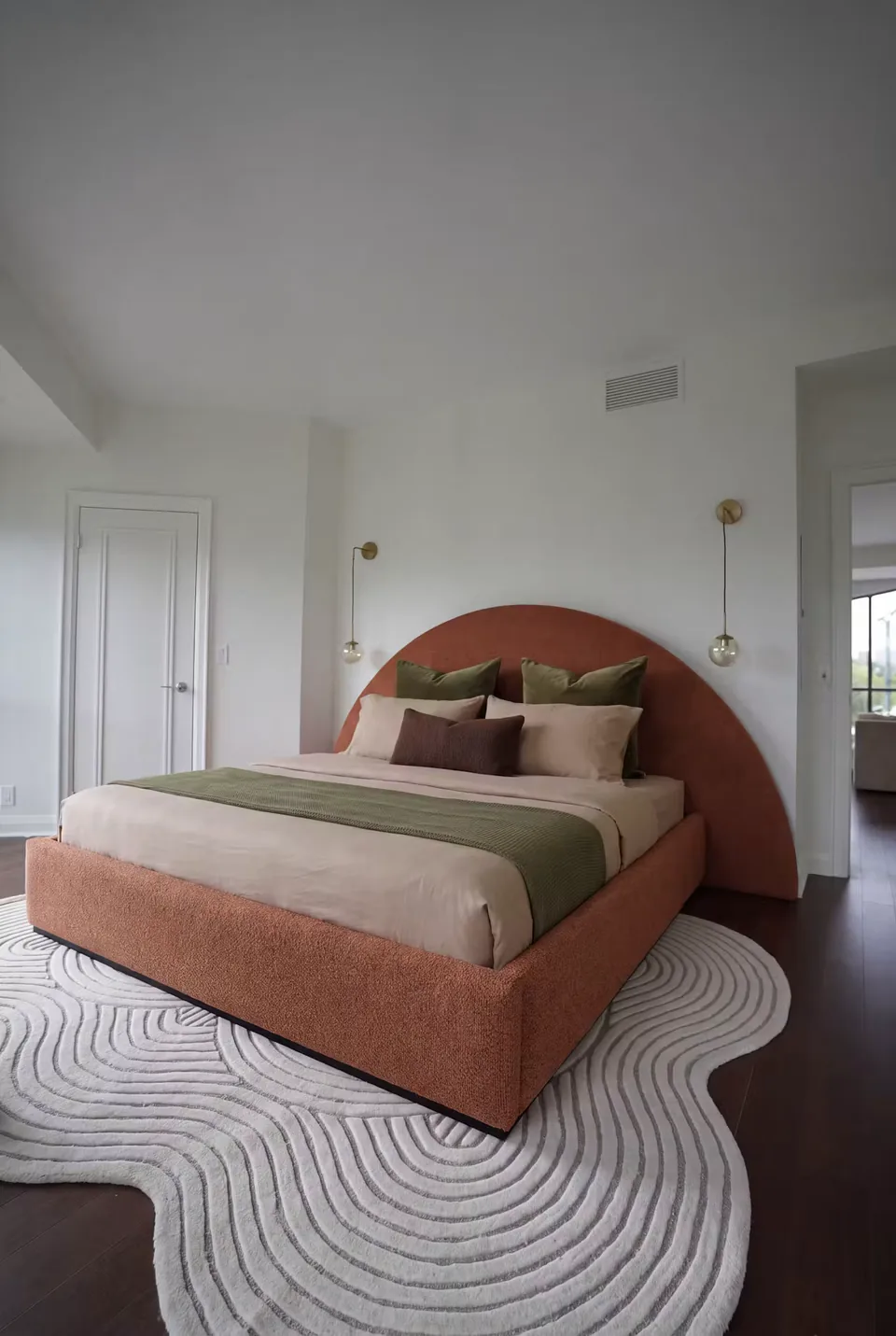 Full room view of the curved terracotta bed above a circular-patterned rug