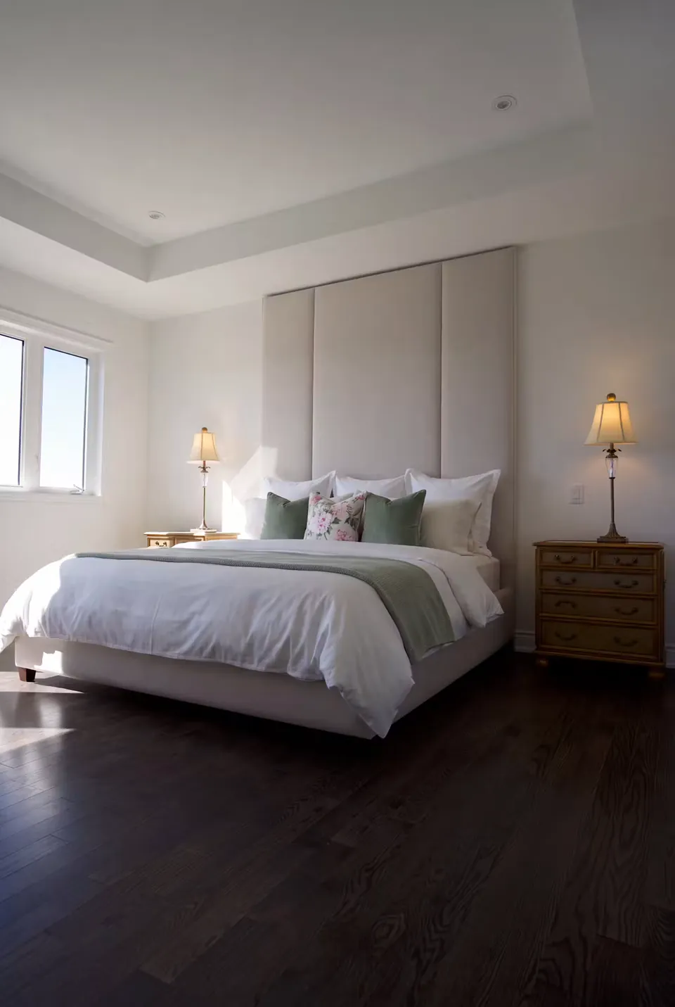 Full angled view of a warm-grey upholstered bed beneath broad tall panels and green cushions.