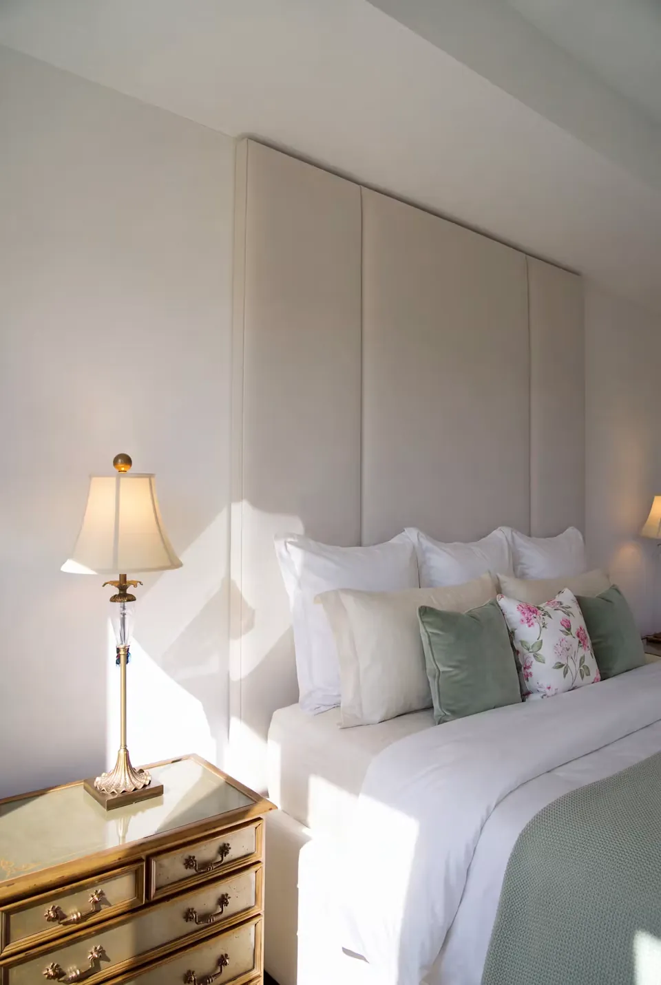 Close view of pale bedding, a green floral cushion and a bedside lamp.