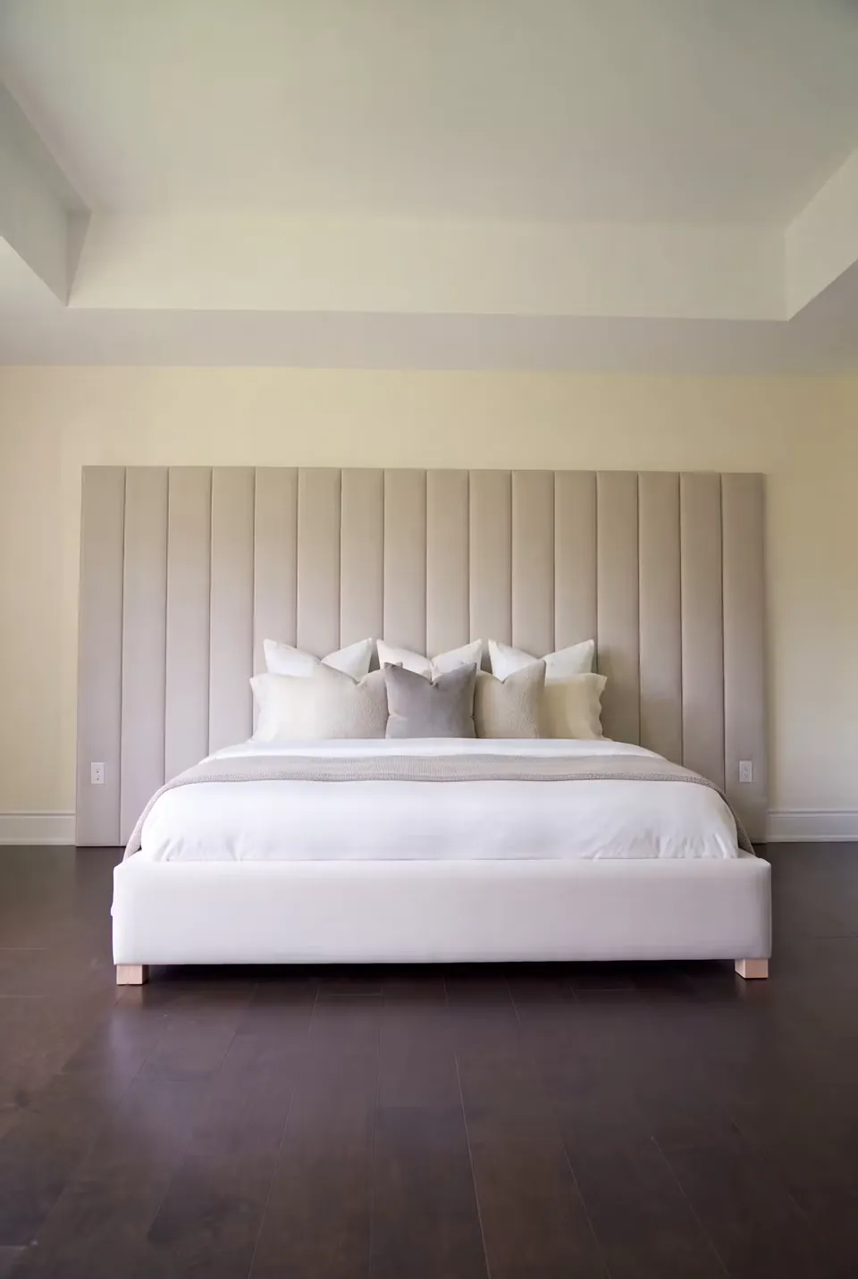 Front view of the white bed and channelled headboard above dark timber flooring.