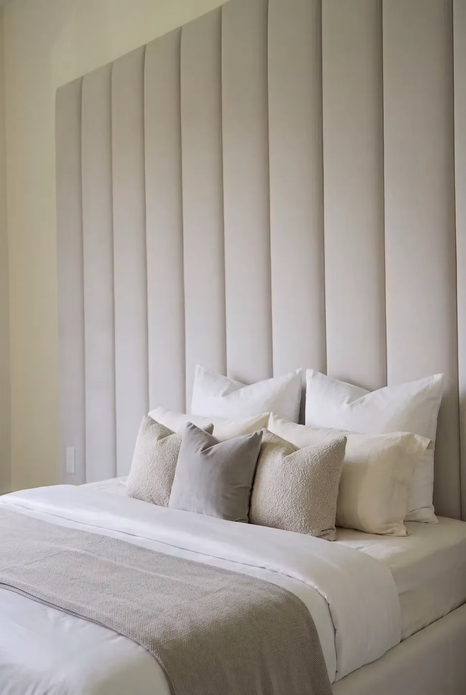 Close angled view of white bedding against pale vertical wall padding.