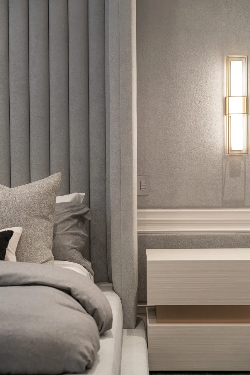 Grey headboard channels beside a pillow, bedside table and brass-coloured wall light